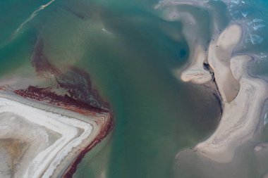 Tenha bir plajın güneşli bir günde turkuaz suyla nazikçe örtüldüğü hava manzarası.