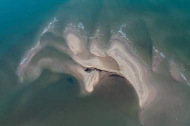 Tenha bir plajın güneşli bir günde turkuaz suyla nazikçe örtüldüğü hava manzarası.