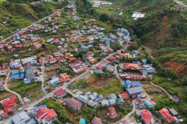 Tarımsal terasların havadan görünüşü geometrik desenler yaratıyor, çiftlik evleri ve kırsal bir alanda dolambaçlı toprak bir yol ile karışıyor.