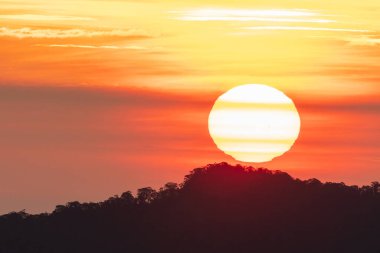 Karanlık bir tepenin ve renkli bir gökyüzünün ardında görünen deseni olan büyük batan güneş.