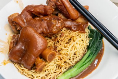 Pişmiş domuz paçası yumurta eriştesi, çubuk ve yanında çorba ile servis edilir.