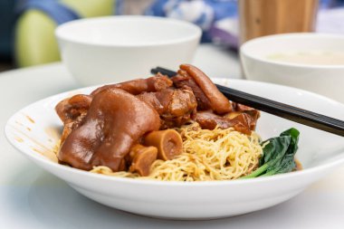 Pişmiş domuz paçası yumurta eriştesi, çubuk ve yanında çorba ile servis edilir.