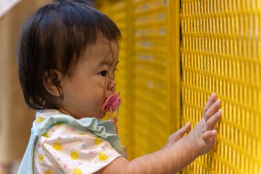 Emzik taşıyan bir kızın yakın çekimi, sarı plastik bir ağa dokunuyor, dokuları ve renkleri keşfediyor.