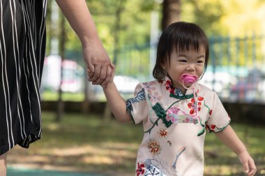 Çekici bir çiçek ve kuş desenli Qipao giymiş bir çocuk, düşünceli bir şekilde parkın manzarasına bakıyor..