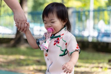 Çekici bir çiçek ve kuş desenli Qipao giymiş bir çocuk, düşünceli bir şekilde parkın manzarasına bakıyor..