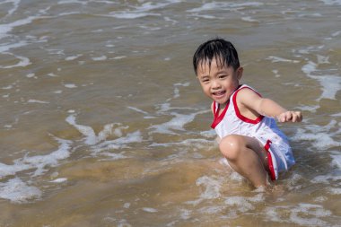 Çocuk sıcak deniz suyuyla sahilde oynamaktan zevk alıyor.