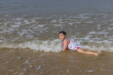 Çocuk sıcak deniz suyuyla sahilde oynamaktan zevk alıyor.