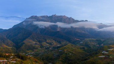 Şafak vakti Majestic Dağı Kinabalu bulutların üzerinde yükselir, Sabah, Borneo 'daki Kundasang vadisine tepeden bakar.