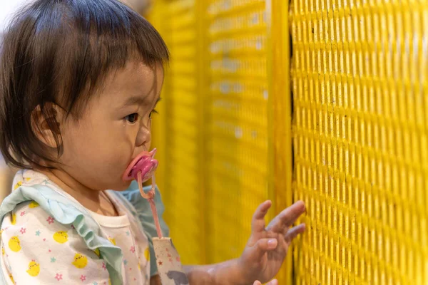 Emzik taşıyan bir kızın yakın çekimi, sarı plastik bir ağa dokunuyor, dokuları ve renkleri keşfediyor.