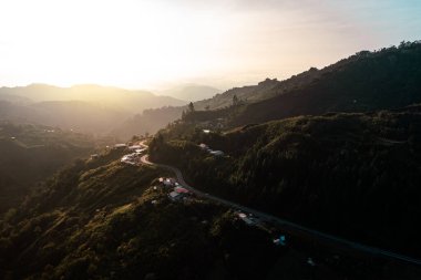 Kıvrımlı, yeşil dağların arasından kıvrılarak geçen, güneşin altın ışığıyla aydınlatılan, dolambaçlı bir yolun nefes kesici manzarası.