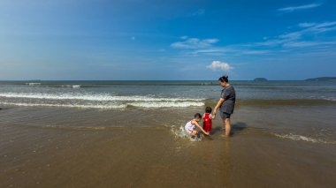 Yumuşak dalgalarda aile eğlencesi. Bir anne ve çocukları su sıçratır ve dalgalarda oynarlar..
