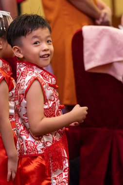 Genç bir çocuk, neşeyle parıldıyor, geleneksel Çin kıyafetleri giyiyor..