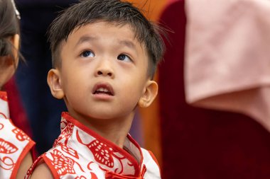 Genç bir çocuk, neşeyle parıldıyor, geleneksel Çin kıyafetleri giyiyor..