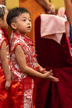 Genç bir çocuk, neşeyle parıldıyor, geleneksel Çin kıyafetleri giyiyor..