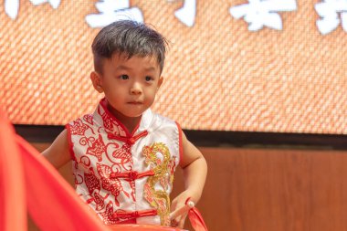 Genç bir çocuk, neşeyle parıldıyor, geleneksel Çin kıyafetleri giyiyor..