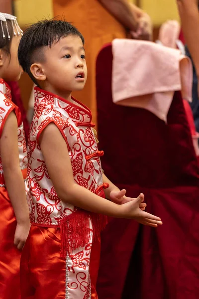 Genç bir çocuk, neşeyle parıldıyor, geleneksel Çin kıyafetleri giyiyor..