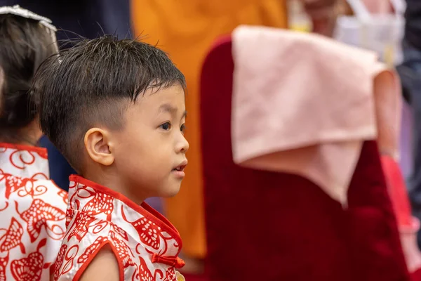 Genç bir çocuk, neşeyle parıldıyor, geleneksel Çin kıyafetleri giyiyor..