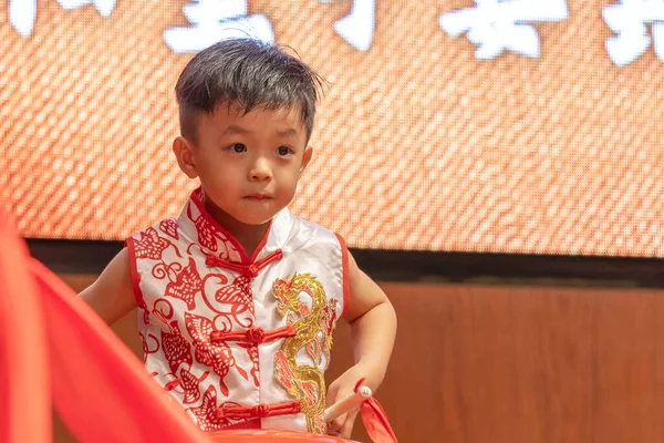 Genç bir çocuk, neşeyle parıldıyor, geleneksel Çin kıyafetleri giyiyor..
