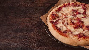 Mozzarella 'lı ev yapımı pizza ve fesleğenli jambon. Tahta bir masanın üstünde..