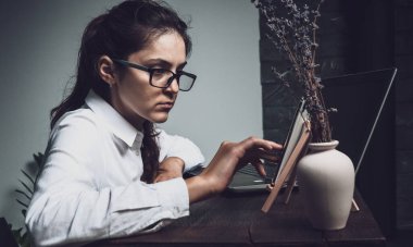 Gözlüklü kız evde bilgisayarla çalışıyor ve çevrimiçi yayın yapıyor. Tahta masadaki kız. Yaratıcı kız.  