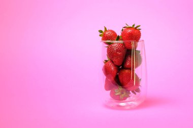 Çilekler bir kasede suludur. Pembe bir arka planda.