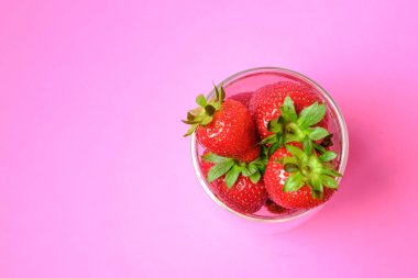 Çilekler bir kasede suludur. Pembe bir arka planda.