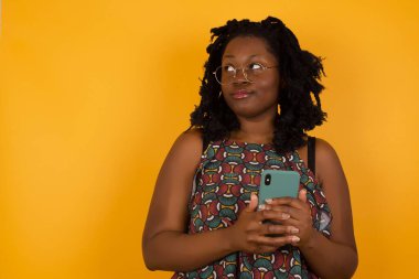  Sarı arka planda gözlük takan güzel afro-amerikalı kadın, el ele tutuşuyor, iyi gençlik haberleri okuyor, boş uzay reklamları yapıyor, kırmızı gömlek giyiyor, izole edilmiş beyaz arka plan giyiyor.