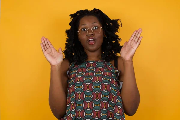 Şaşırmış genç, Afro-Amerikalı, gözlük takan, belirsiz hareketler yapan, kameraya bakan, şaşırmış, hileli soruya cevap veremeyen, sarı arka planda izole edilmiş güzel bir kadın. İnsanlar, vücut dili, duygu kavramı