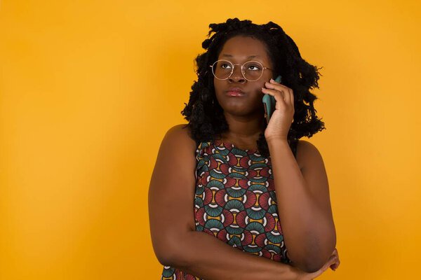 Sad Young beautiful afro american woman wearing glasses over yellow background talking on smartphone on yellow background. Communication concept.
