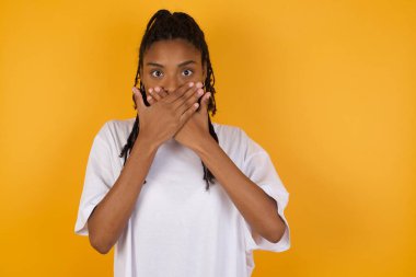 Korkmuş Afrikalı Amerikalı kadın sarı arka plana ve ağzı kapalı 