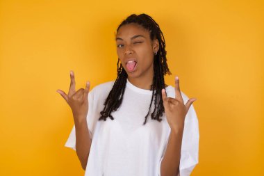 Afrikalı Amerikalı kadın sarı arka planda rock hareketi yapıyor. 