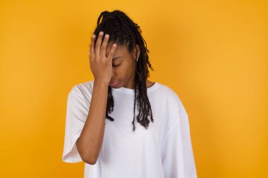 Sarı arka planda elleri alnında Afrikalı Amerikalı bir kadın. 