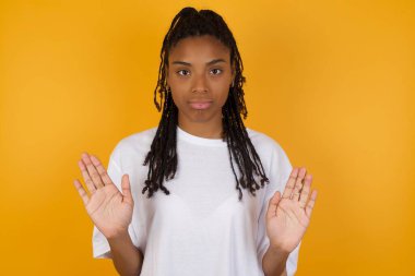 Afro-Amerikalı kadın avuç içlerini kameraya çekiyor, jestleri durdurup duygularını kontrol etmek ve sarı arka planda gerilmemek istiyor. 