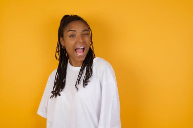 Gülümseyen Afrikalı Amerikalı kadın sarı arka planda göz kırpıyor. 
