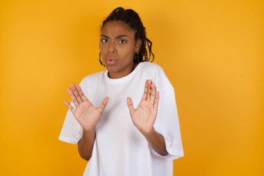 Korkak Afrikalı Amerikalı kadın sarı arka planda avuçlarını açık tutuyor. 