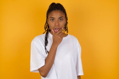 Korkak Afrikalı Amerikalı kadın, sarı arka plana karşı elleri çenesinde 