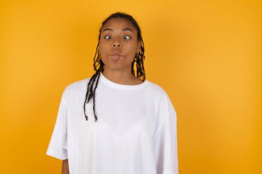 Afrikalı Amerikalı bir kadın sarı arka planda dudaklarını büzüyor. 