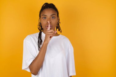 Afrikalı Amerikalı kadın sarı arka planda sessiz olmak istiyor. 