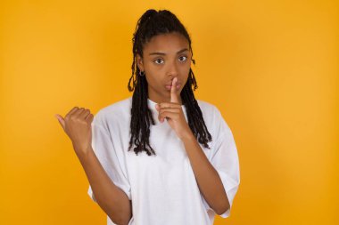 Afrikalı Amerikalı kadın sarı arka planda sessiz olmak istiyor. 