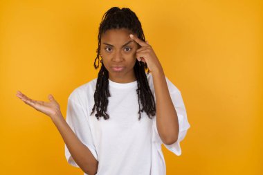 Canı sıkkın Afrikalı Amerikalı kadın sarı arka planda alnını işaret ediyor.