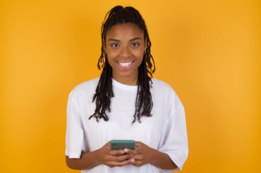 Saçları örgülü, günlük giysiler giyen, uzak iletişimden hoşlanan, cep telefonu kullanan, hızlı, sınırsız internet sörfü yapan, hoş bir gülümsemesi olan, kırmızı tişörtlü, online alışveriş yapan koyu renk saçlı genç bir kadın., 