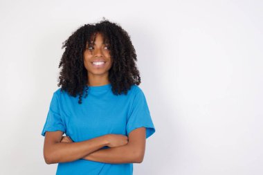 Rüya gibi istirahat kıvırcık saçlı, sıradan mavi gömlekli, beyaz arka planda kollarını kavuşturan Afrikalı bir kadın iyi görünüyor. 