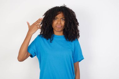 Mutsuz, kıvırcık saçlı, günlük mavi gömlekli, beyaz arka planda duran Afrikalı bir kadın intihar jesti yapıyor ve tabancayı eliyle taklit ediyor, dudakları kıvrımlı, iki parmağını şakakta tutuyor.