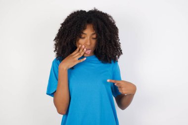 Şok olmuş kıvırcık saçlı, sıradan mavi gömlekli, beyaz arka planda duran genç Afrikalı kadın şaşırtıcı bir şekilde aşağı bakıyor. Korkmuş kadın, lüks mağazadan her zamanki gömleğin fiyatını öğrenir.