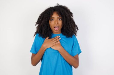 Kıvırcık saçlı, sıradan mavi tişörtlü, korkmuş bakışları olan, göğsüne dokunmuş, garip bir şey fark eden korkmuş Afrikalı bir kadın..