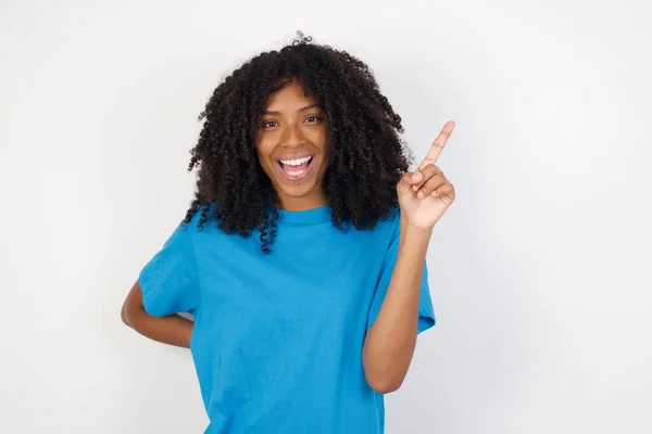 곱슬머리의 아프리카 여자가 파란색 셔츠를 배경에 생각하고 포즈를 취하고 손가락을 — 스톡 사진