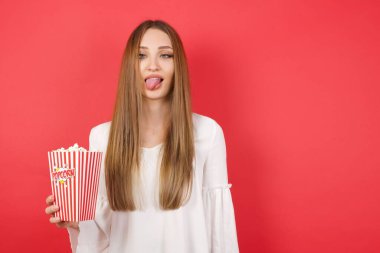 Young beautiful woman with popcorn showing grimace face crossing her eyes and showing tongue . Being funny and crazy clipart