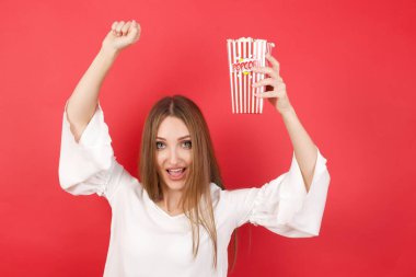 Kırmızı stüdyo arka planında patlamış mısırlı güzel beyaz kadın.