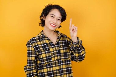 Güzel genç bir kadın bir numarayı gösterip işaret ederken kendinden emin ve mutlu bir şekilde gülümsüyor..