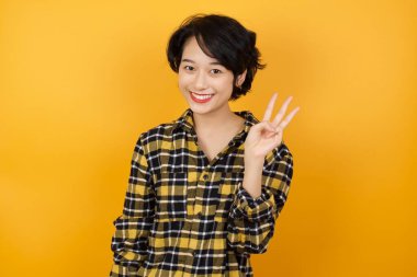 Güzel genç bir kadın kendini beğenmiş ve mutlu bir şekilde gülümserken üç numarayı gösterip işaret ediyor..